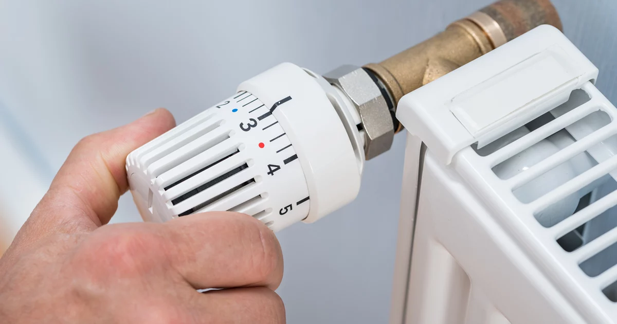 Main réglant un robinet thermostatique sur un radiateur à eau